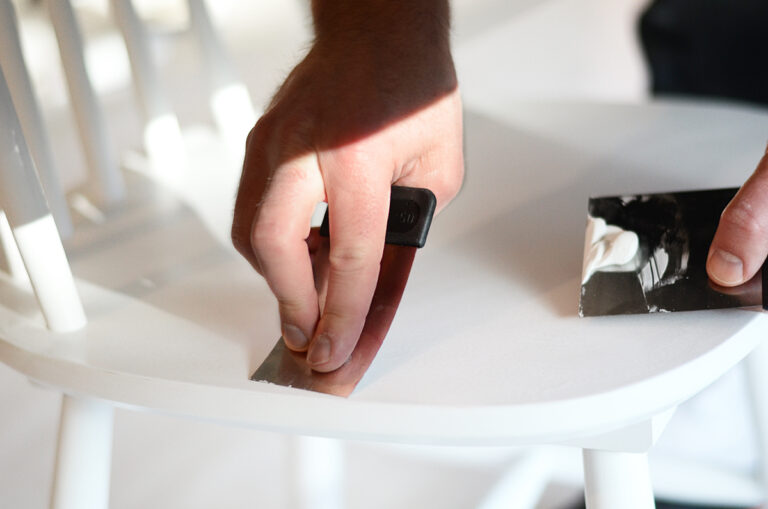 Hand som brer ut spackel på pinnstolen med hjälp av en japanspackel